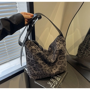 Detail of leopard print tote bag featuring wide black leather strap and metal buckle