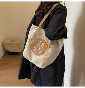 Close-up of canvas tote bag featuring leather patch and cute plush chick keychain accessory
