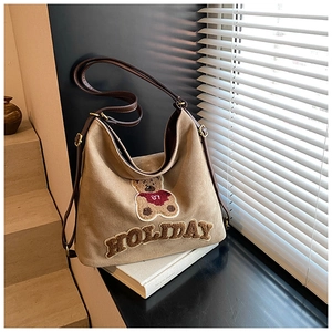 Detail of vintage beige shoulder bag featuring plush bear patch and HOLIDAY embroidery