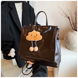Detail of dark brown faux leather backpack with a plush orange cloud charm accessory