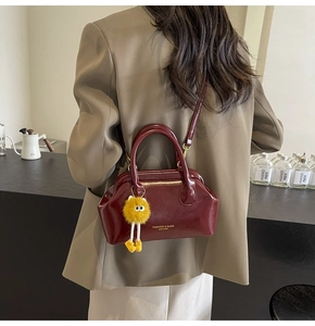 Dettaglio borsa Boston lucida bordeaux con logo dorato e ciondolo pompon giallo vivo