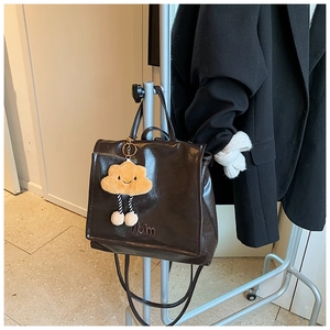 Detailed view of glossy dark brown backpack with yellow plush cloud charm on hanger