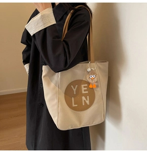 Close-up of minimalist canvas tote with leather patch and plush bird charm detail