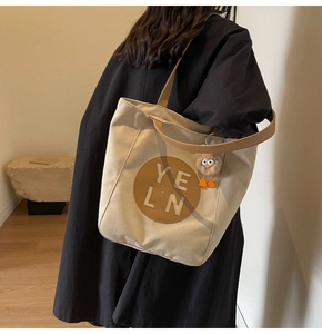 Detail of large canvas tote bag with brown leather handles and plush eye charm accessory