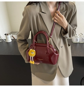 Dettaglio borsa in pelle bordeaux con scritte moda e ciondolo a pompon giallo