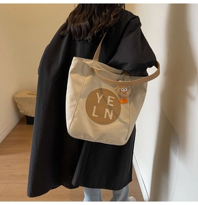 Detailed back view of a person wearing a beige canvas tote bag with a cartoon charm