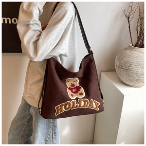 Detail of dark brown suede tote bag with teddy bear patch worn by model over shoulder