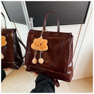 Detail of dark brown glossy leather backpack with cute cloud plush charm and embossed logo