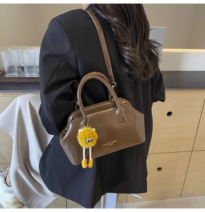 Dettaglio borsa a mano in pelle marrone con ciondolo di pelliccia e tracolla sottile
