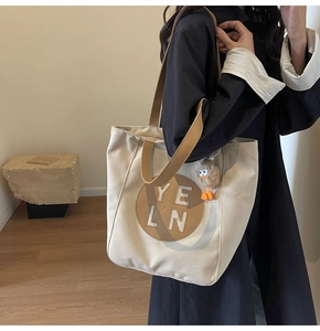 Detail of canvas tote bag featuring leather patch and cute bird plush charm accessory