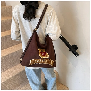 Brown suede hobo bag with teddy bear embroidery shown worn over the shoulder