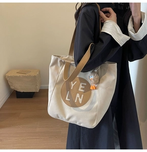 Detail of canvas tote bag featuring brown leather logo patch and fuzzy charm accessory