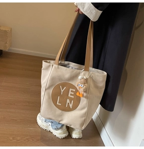 Close-up of canvas tote bag with brown leather handles and a plush bird charm detail