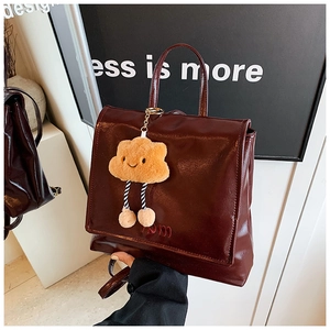 Detail of dark red vintage backpack with embroidered text and plush cloud charm