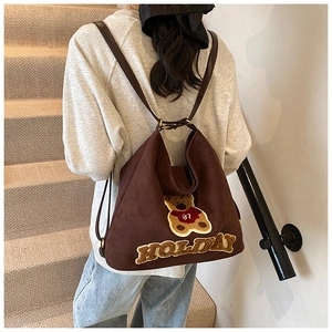 Detail of a brown canvas backpack featuring a plush bear patch and leather straps
