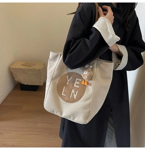 Detail of canvas tote bag with brown leather patch and plush bird charm on female model