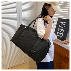 Black large capacity travel tote bag with reinforced handles on a model in a bright setting