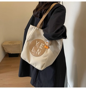 Detailed view of canvas tote bag with brown leather patch and cute bird charm