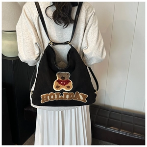 Detail of a black suede backpack with teddy bear embroidery and HOLIDAY lettering patch
