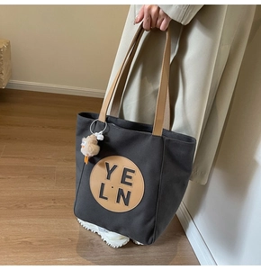 Detail of charcoal grey canvas tote bag with brown leather straps and plush bird charm