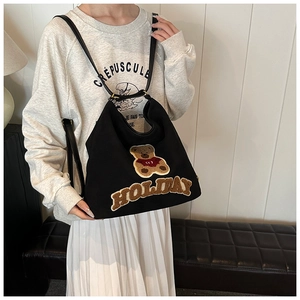 Close-up of black canvas tote bag with brown teddy bear patch and HOLIDAY text