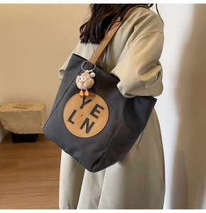 Model carrying a charcoal canvas tote bag with brown leather patch and yellow duck charm