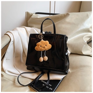 Detail of glossy black leather backpack with a cute plush cloud charm and top handle