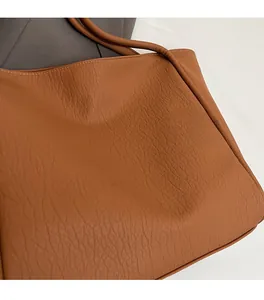 Close-up of brown faux leather tote bag showing soft lychee grain texture and handle