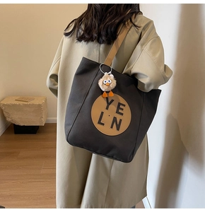 Detailed view of large grey canvas tote bag with brown leather patch and plush charm