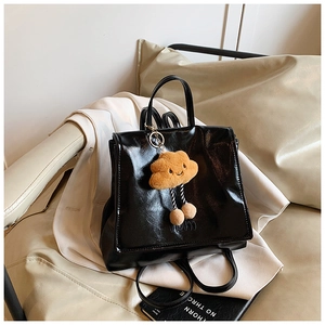 Detail of glossy black leather backpack with cute cloud charm on soft white sofa
