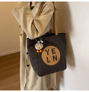 Detail view of large charcoal canvas tote bag with brown straps and plush monster charm