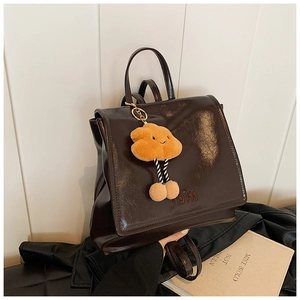 Detail of glossy brown leather backpack with 'mom' logo and yellow plush cloud charm