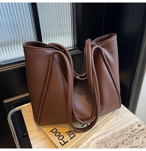 Detailed view of coffee brown tote bag with premium lychee grain texture on a book