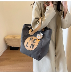 Close-up of charcoal grey canvas tote bag featuring brown leather handles and a plush charm