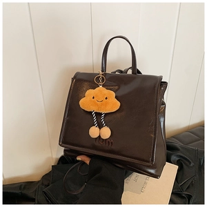Detail view of vintage dark brown leather backpack with cute yellow cloud plush charm