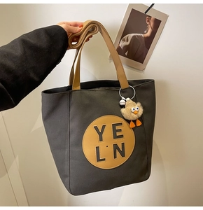 Close-up of grey canvas tote with brown leather strap and cute duck plush charm