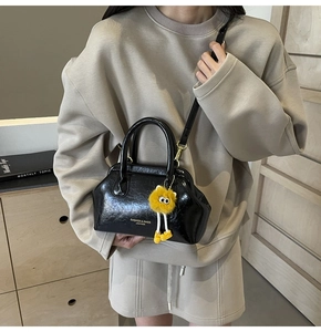 Dettaglio borsa a mano nera in pelle con logo dorato e ciondolo mostro di peluche giallo