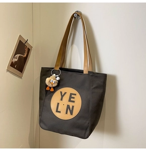 Close-up of grey canvas tote bag with leather patch and plush chick pendant accessory