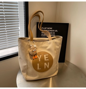 Detail of beige canvas tote bag with brown leather straps and yellow duck plush charm