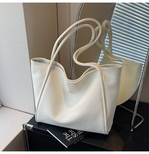 Detailed close-up of white pebble leather texture on a minimalist tote bag with thin straps