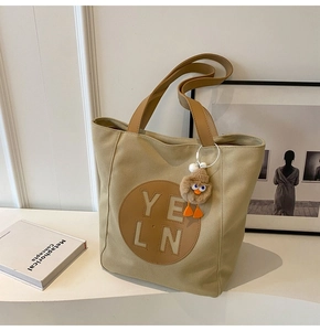 Detail of beige canvas tote bag with leather straps and a plush duck charm accessory