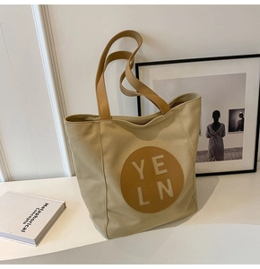 Detail of beige canvas tote bag with brown leather patch and yeln brand lettering