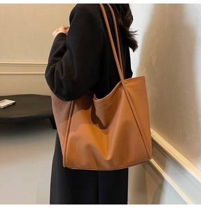 Detail view of a vintage tan faux leather tote bag with pebble texture on a female model