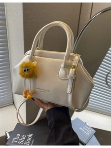 Elegante borsa a tracolla crema con ciondolo mostro e scritte dorate in un set di lifestyle