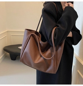 Side view of a large brown pebble grain leather tote bag worn on a woman's shoulder