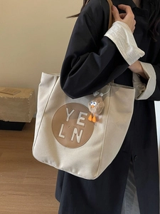 Minimalist beige canvas tote bag with leather patch and plush duck charm detail