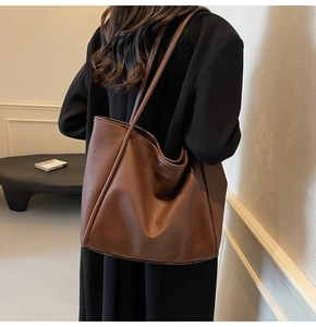 Detail of a large dark brown tote bag with pebble leather texture on a female model