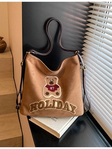 Brown suede tote bag with teddy bear patch and holiday embroidery on a sunny staircase