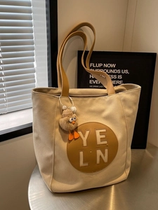 Minimalist beige canvas tote bag with brown leather handles and bird charm on a desk