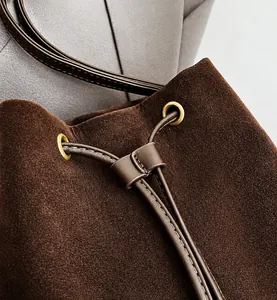 Detail of dark brown suede bucket bag featuring drawstring closure and gold metal eyelets